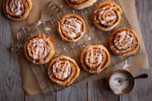 Freshly baked sourdough cinnamon rolls topped with cream cheese frosting on a rustic wooden table.