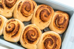 Freshly baked sourdough cinnamon rolls topped with cream cheese frosting on a rustic wooden table.